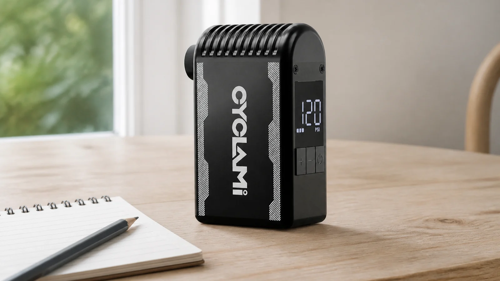 Black compact electric inflator with a digital pressure display standing on a wooden table